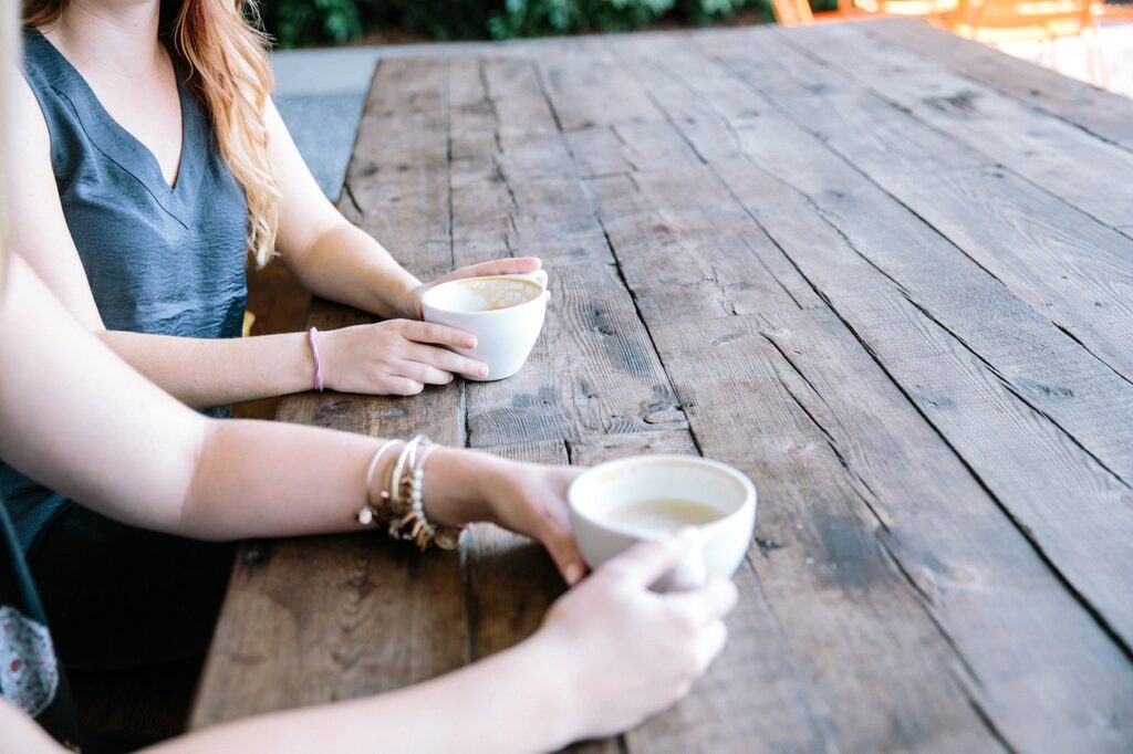 Two people drinking tea or coffee from white cups. Only their hands and arms are visible.